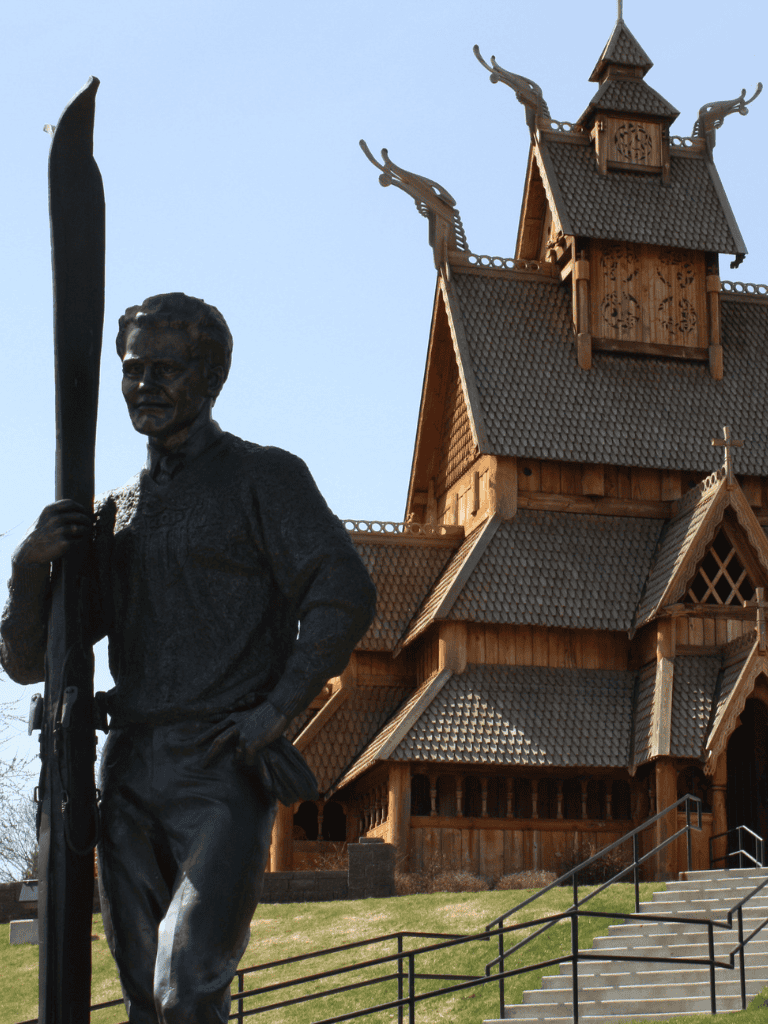 Bronze statue of a man holding a flag in front of a traditional wooden church, illustrating cultural landmarks and heritage.