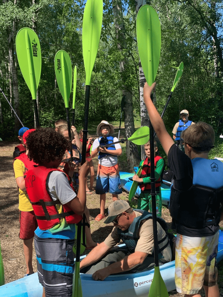Kids learning kayaking with instructor in outdoor wooded setting, adventure and water sports activity.