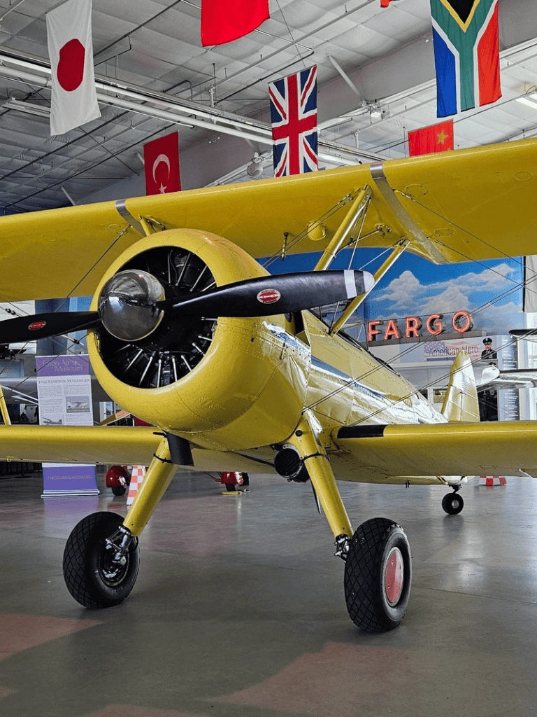 Yellow vintage airplane at aviation museum with international flags, showcasing historical aircraft exhibits.