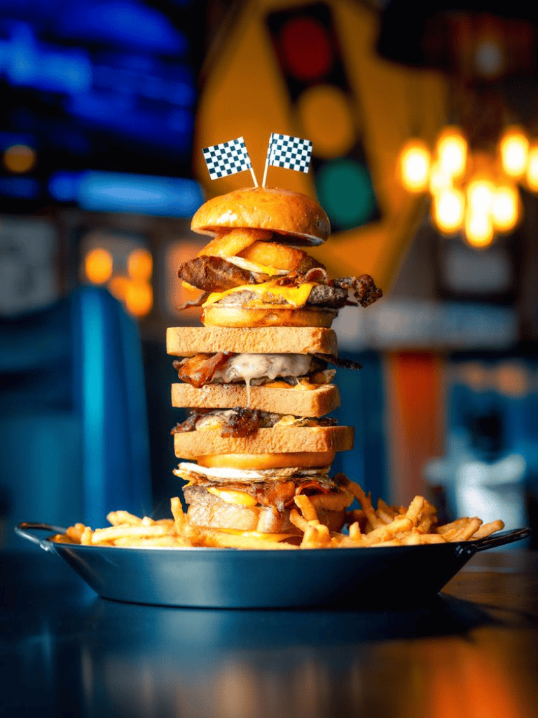 Juicy towering burger with fries and checkered flags at a restaurant, food photography.