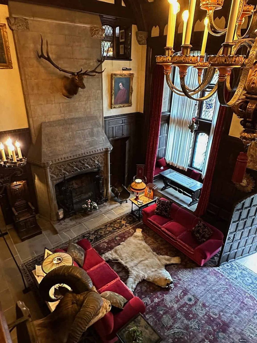 Antique inspired grand living room with fireplace, ornate chandelier, rich red velvet furniture, and classic artwork.