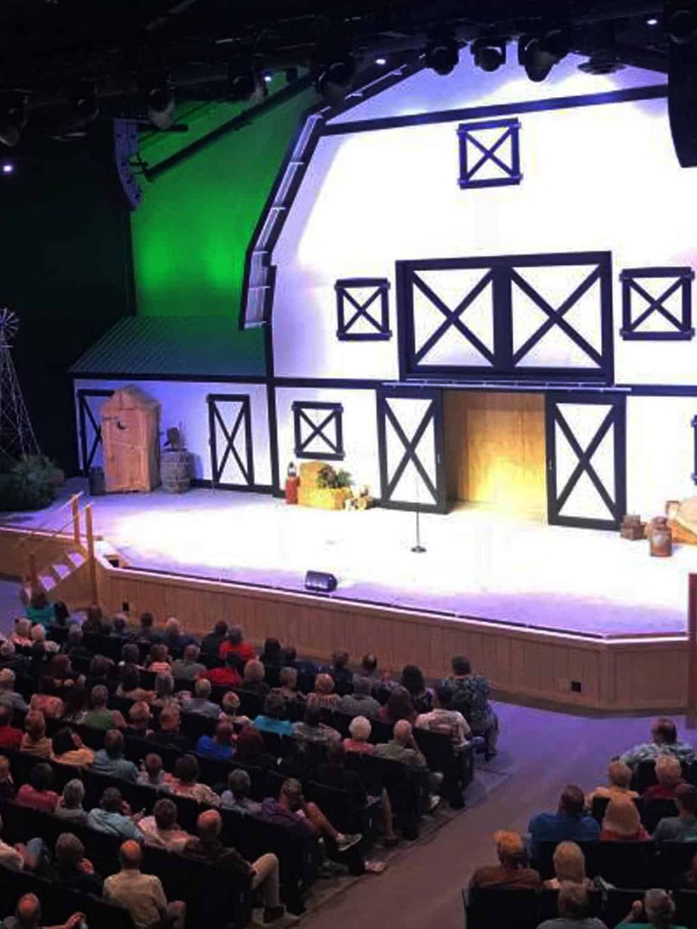 Vibrant theater stage with barn-themed set design for a comedy show and a full audience watching.