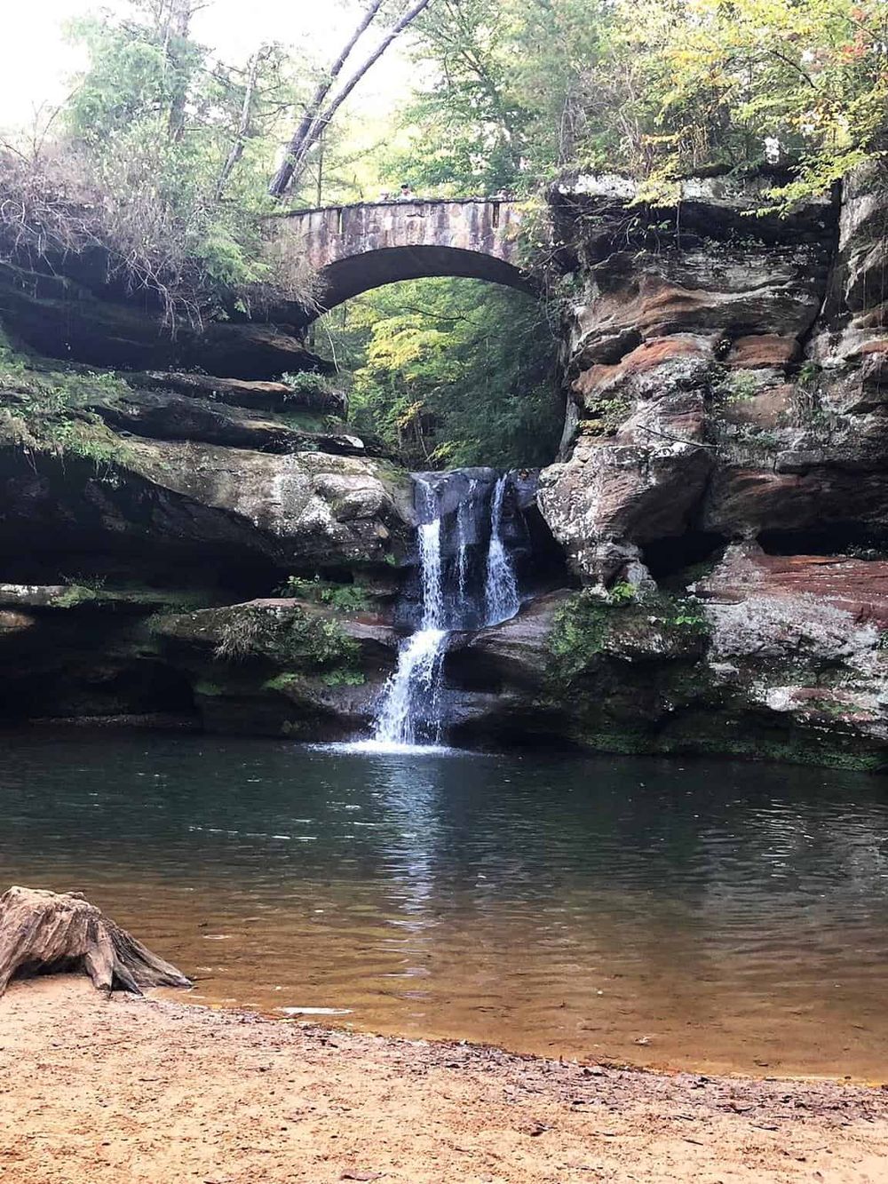 Secluded waterfall with stone bridge in lush forest, ideal for outdoor adventure and scenic exploration.