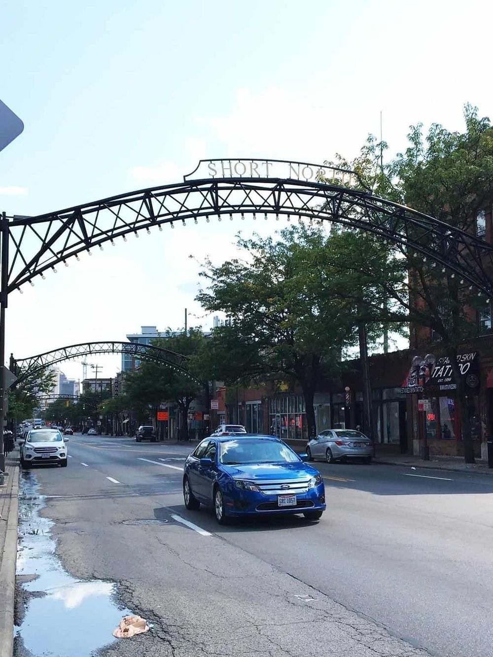 Colorful street scene with historic archway, cars, and trees in an urban downtown setting.