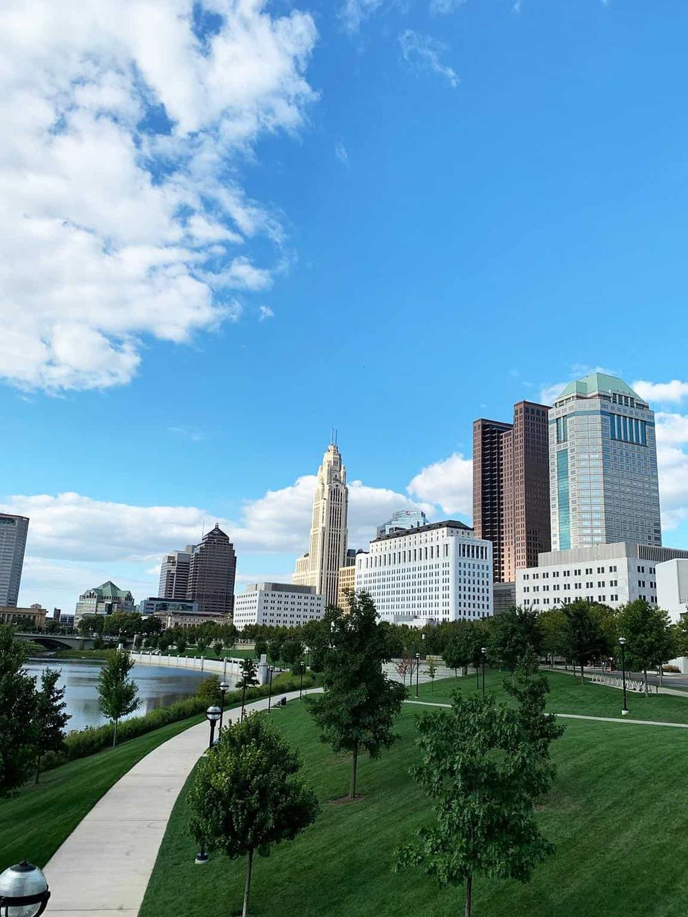 Cityscape of downtown Columbus Ohio with skyscrapers, green park, and river under a blue sky.