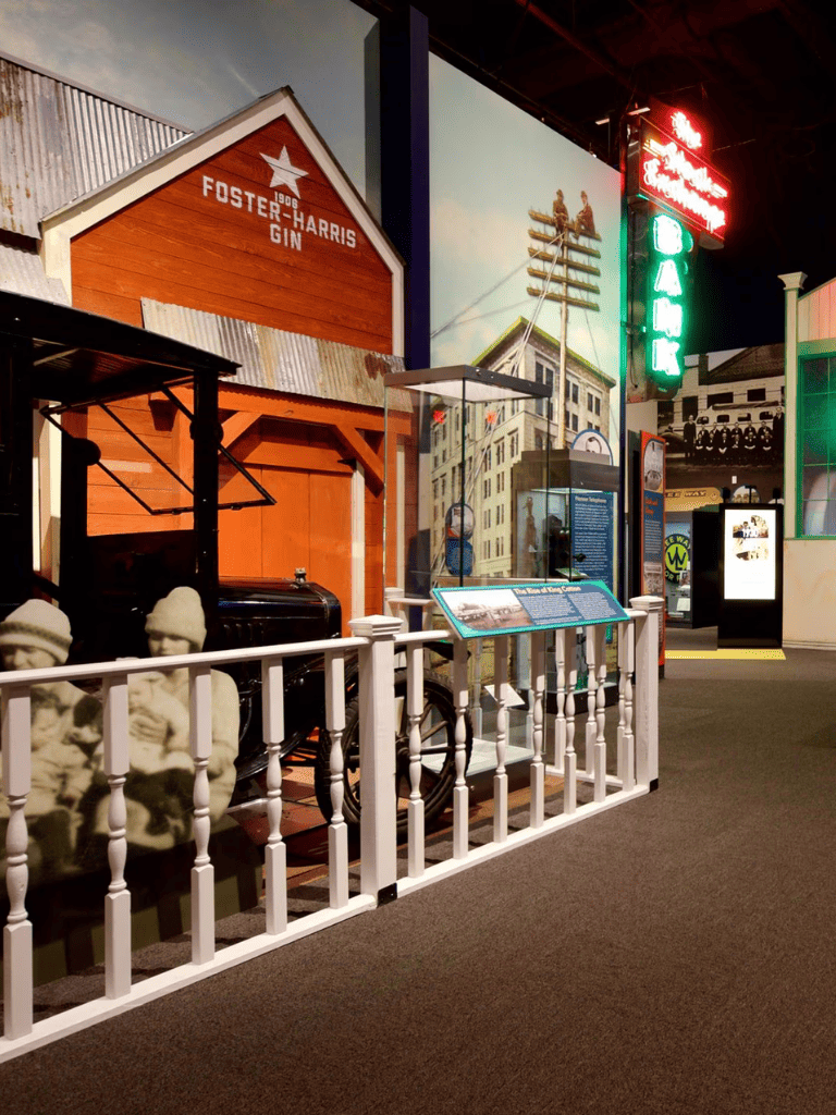 Historic factory building replica with black piano, mannequins, and informational displays at museum exhibit.