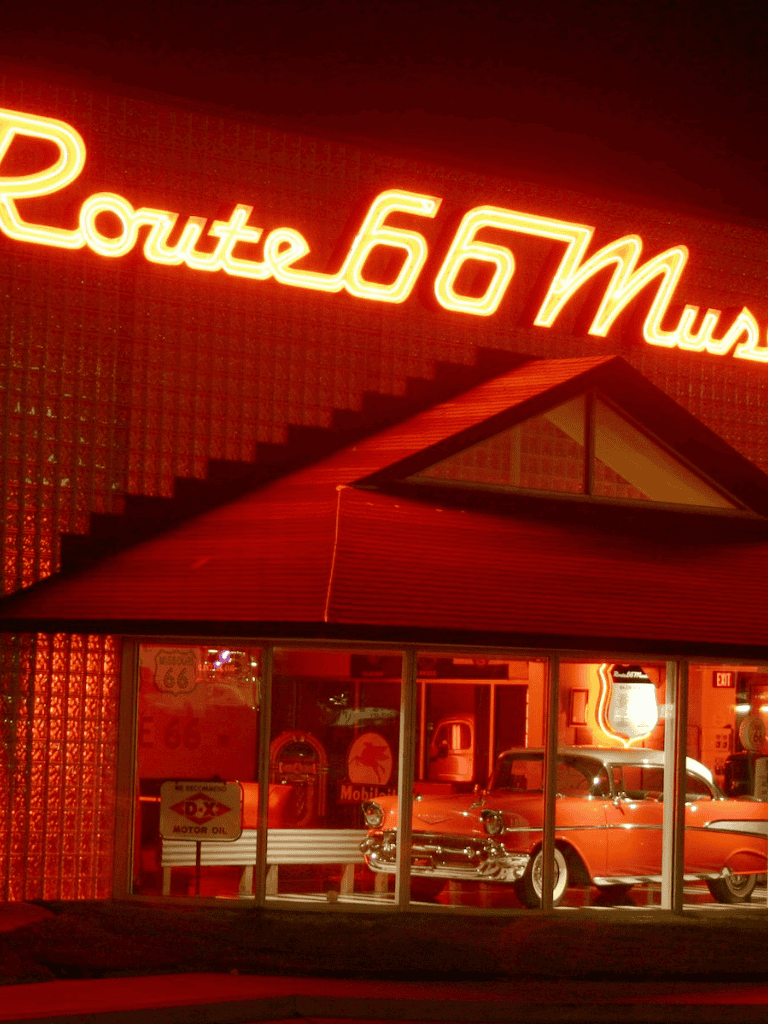 Route 66 neon sign at night in a vintage diner setting, classic cars, nostalgic American road trip vibe.