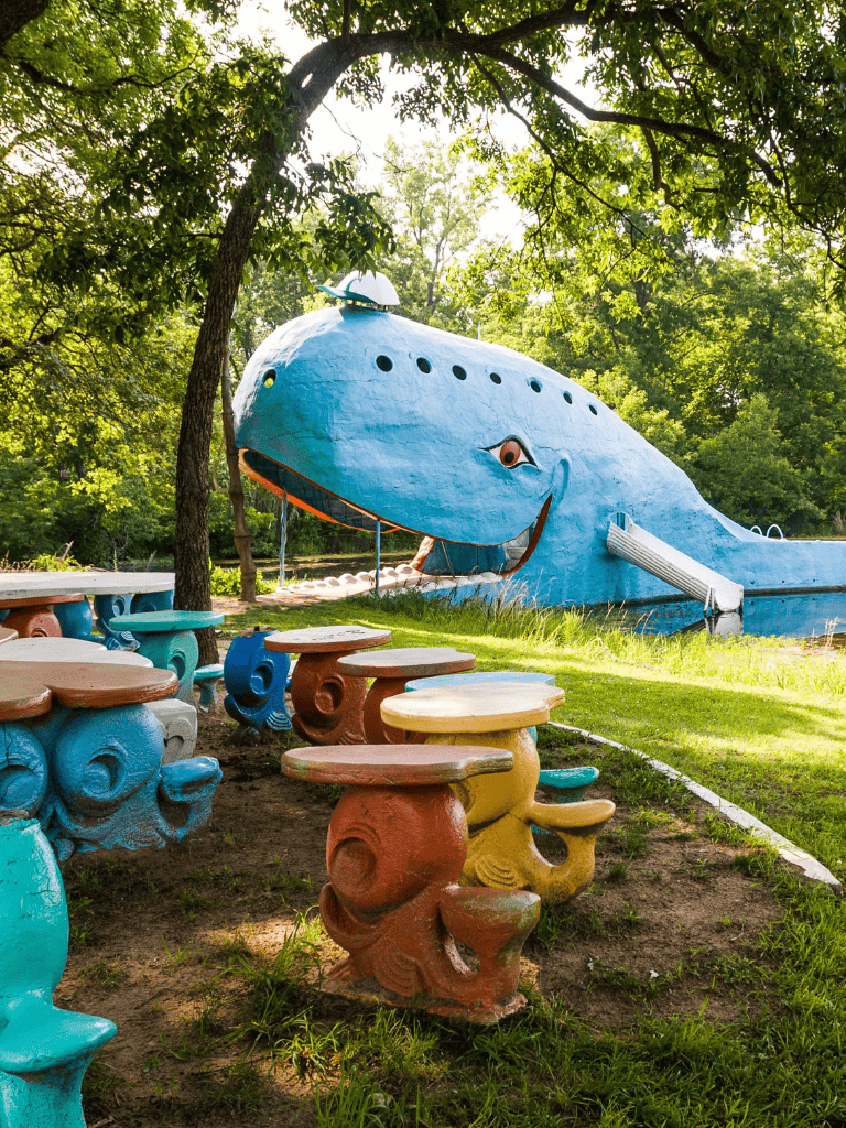 Whimsical whale sculpture with colorful mushroom-shaped seating in a lush park setting.