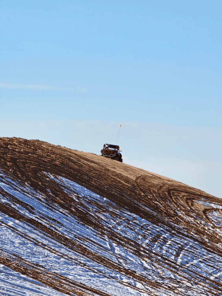 Climbing rugged mountain terrain with off-road vehicle, snow and clear sky in background.