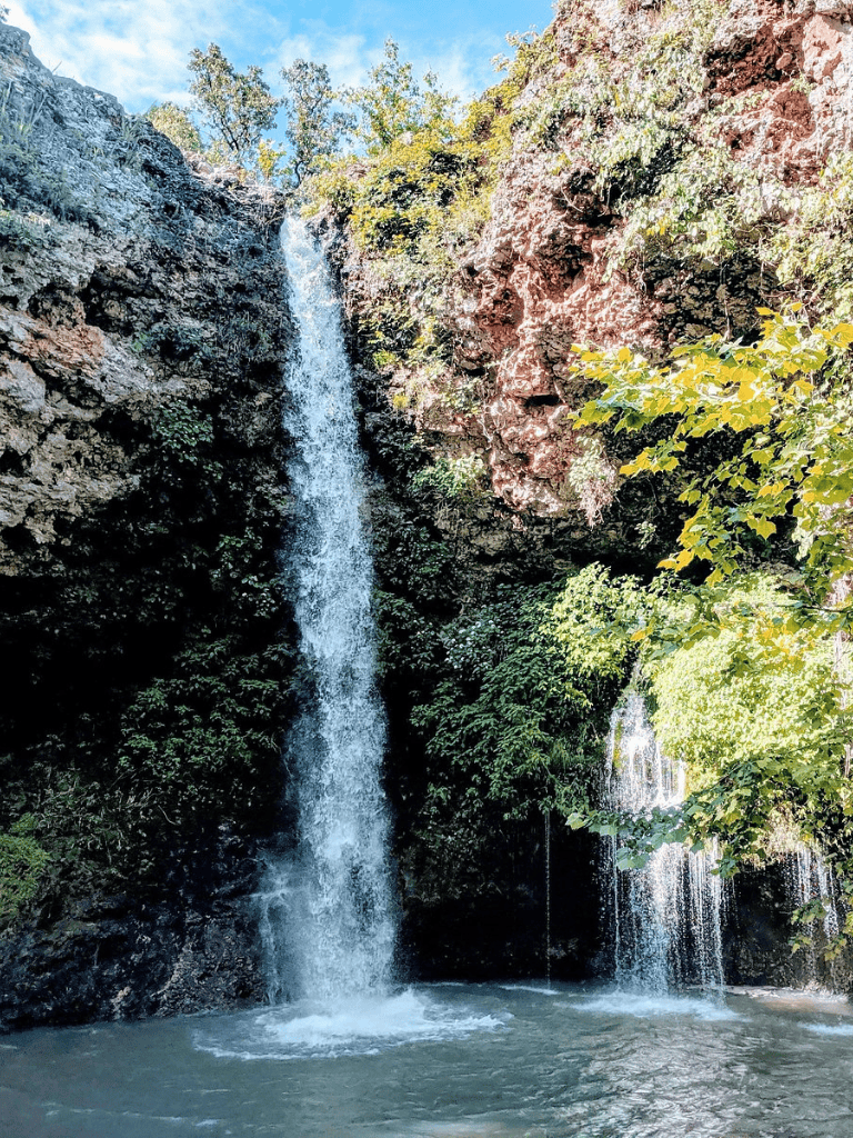 Serene waterfall surrounded by lush greenery and rocky cliffs in a tranquil natural setting.