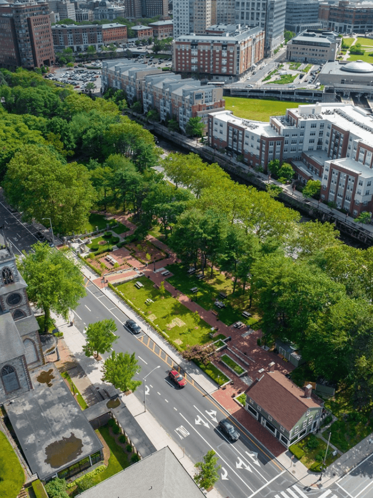 Green city park with trees, pathways, and nearby urban buildings, offering a peaceful outdoor space.