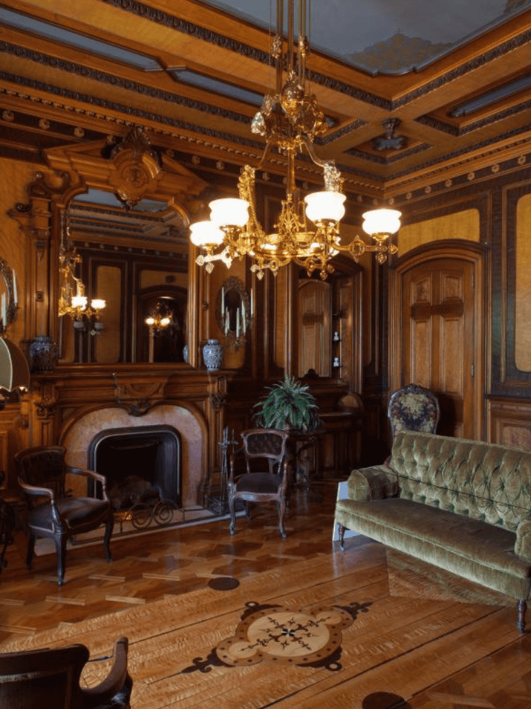 Elegant Victorian living room with ornate wood paneling, antique furniture, and luxurious chandelier.