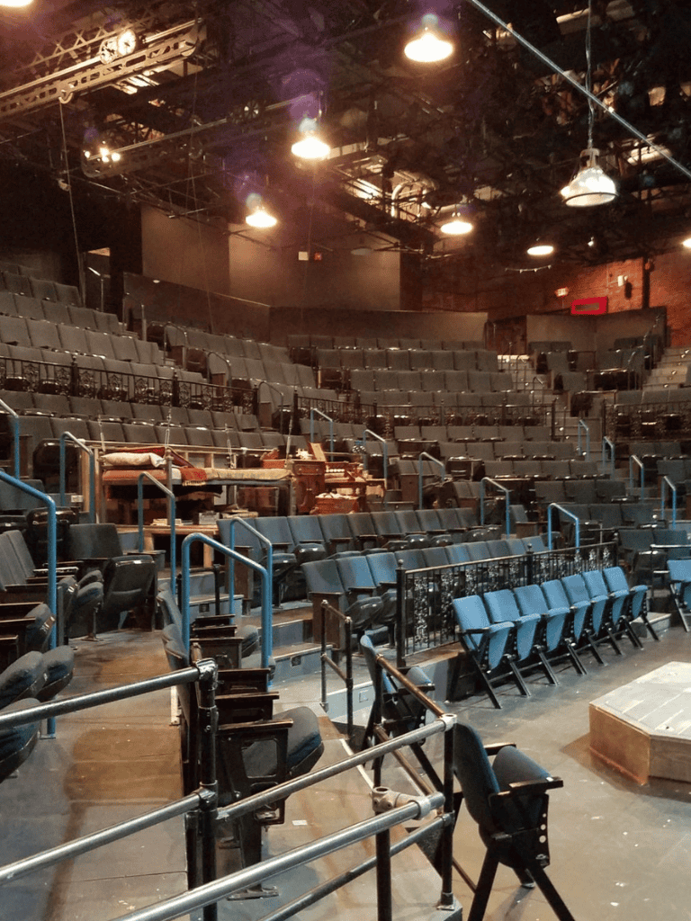 Empty theater auditorium with rows of seats, stage, and lighting setup for a performance or event.