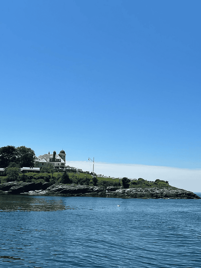 Historic waterfront mansion on rocky coastline under clear blue sky, popular for scenic views and tours.