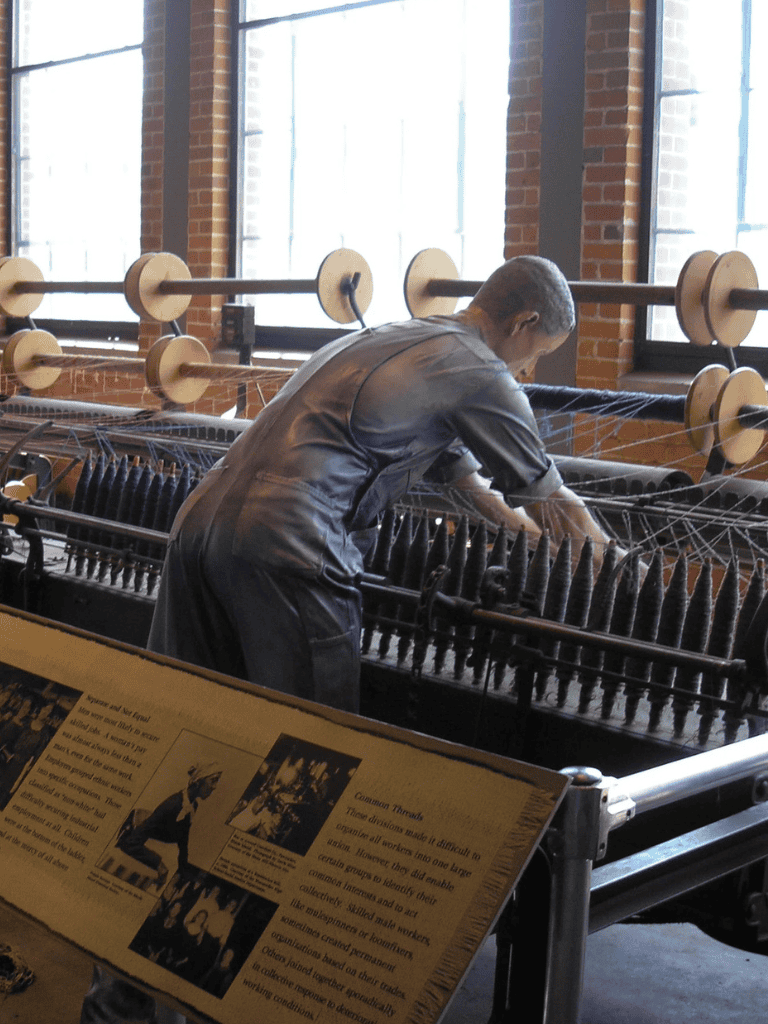 Historic textile mill worker operating a loom in an industrial museum setting.