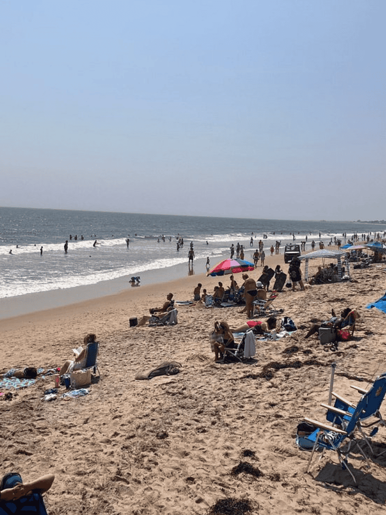 Beach with people relaxing and swimming, sunny day, ideal for seaside adventures and outdoor activities.