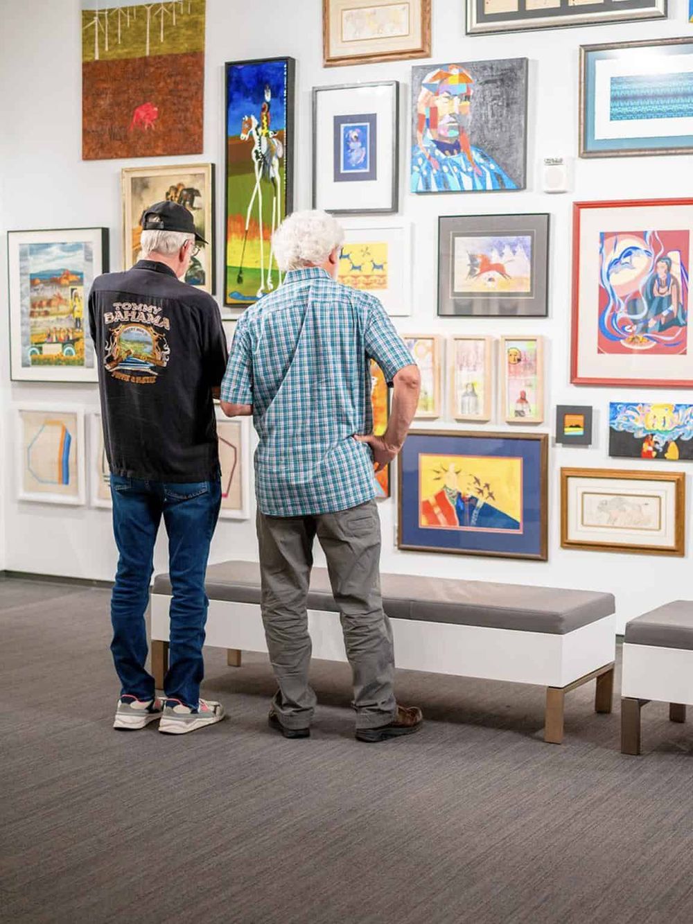 Colorful art gallery with two seniors admiring vibrant paintings and framed artwork on the wall.
