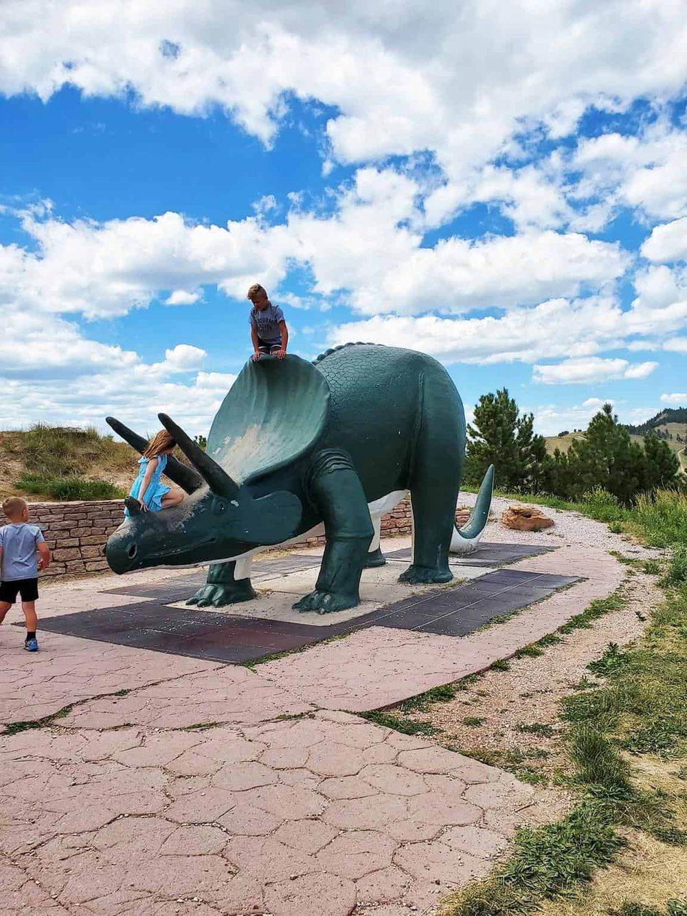 Colorful outdoor sculpture of a triceratops dinosaur in a park setting with children playing.