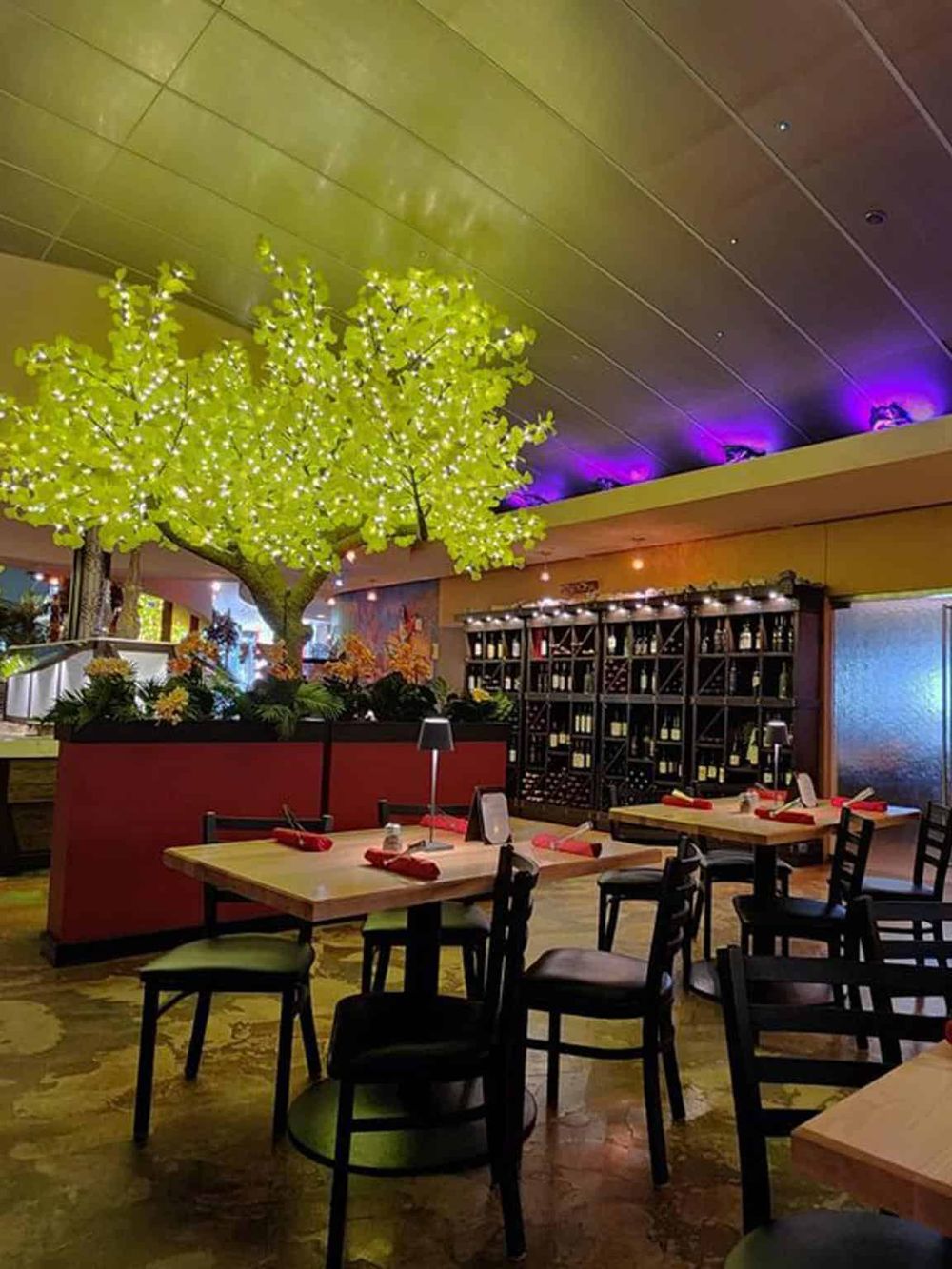 Illuminated decorative tree in a stylish restaurant interior with wine storage.