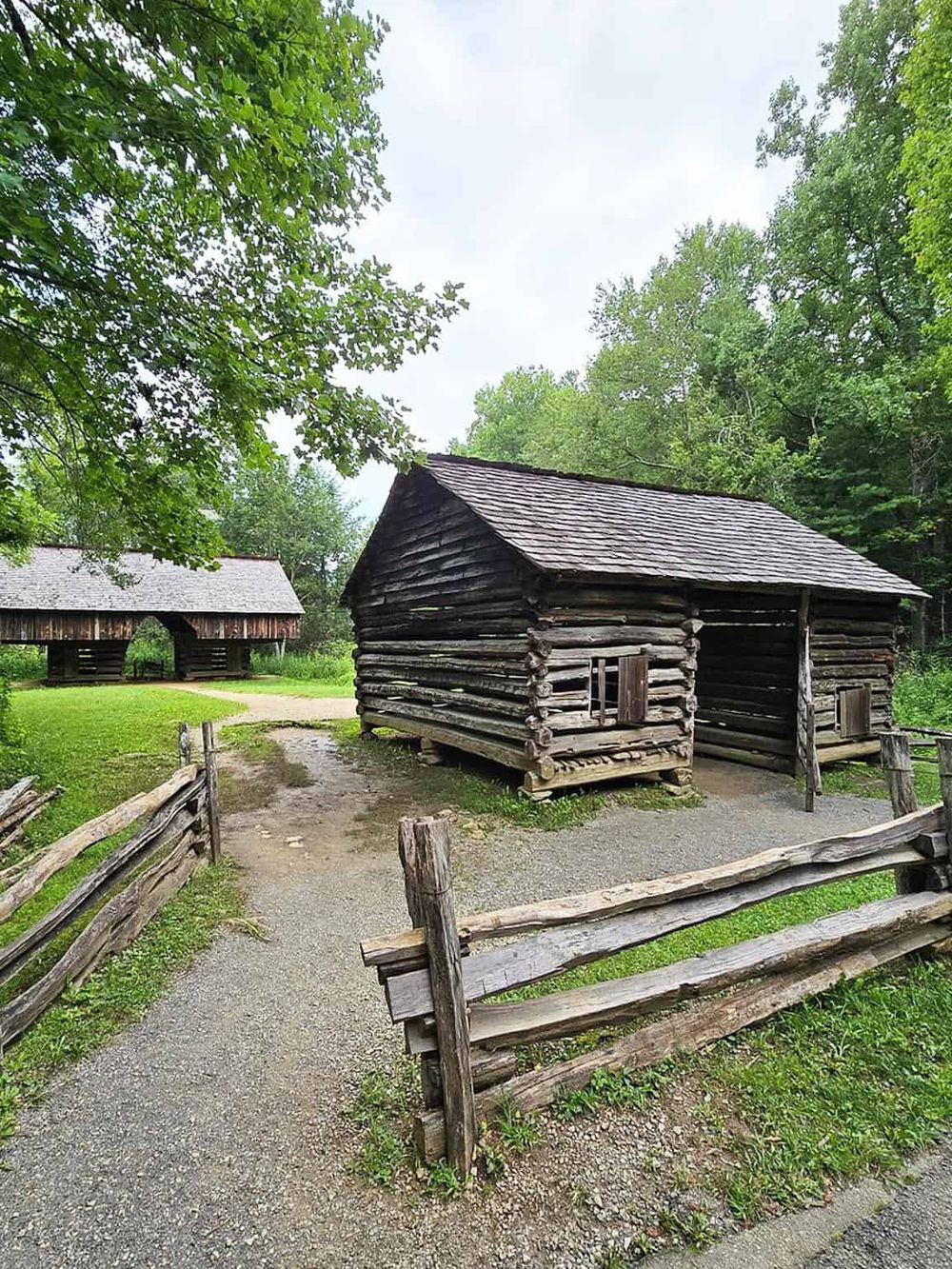 Unfinished log cabin in forest with wooden fences and lush green trees, historic museum site.
