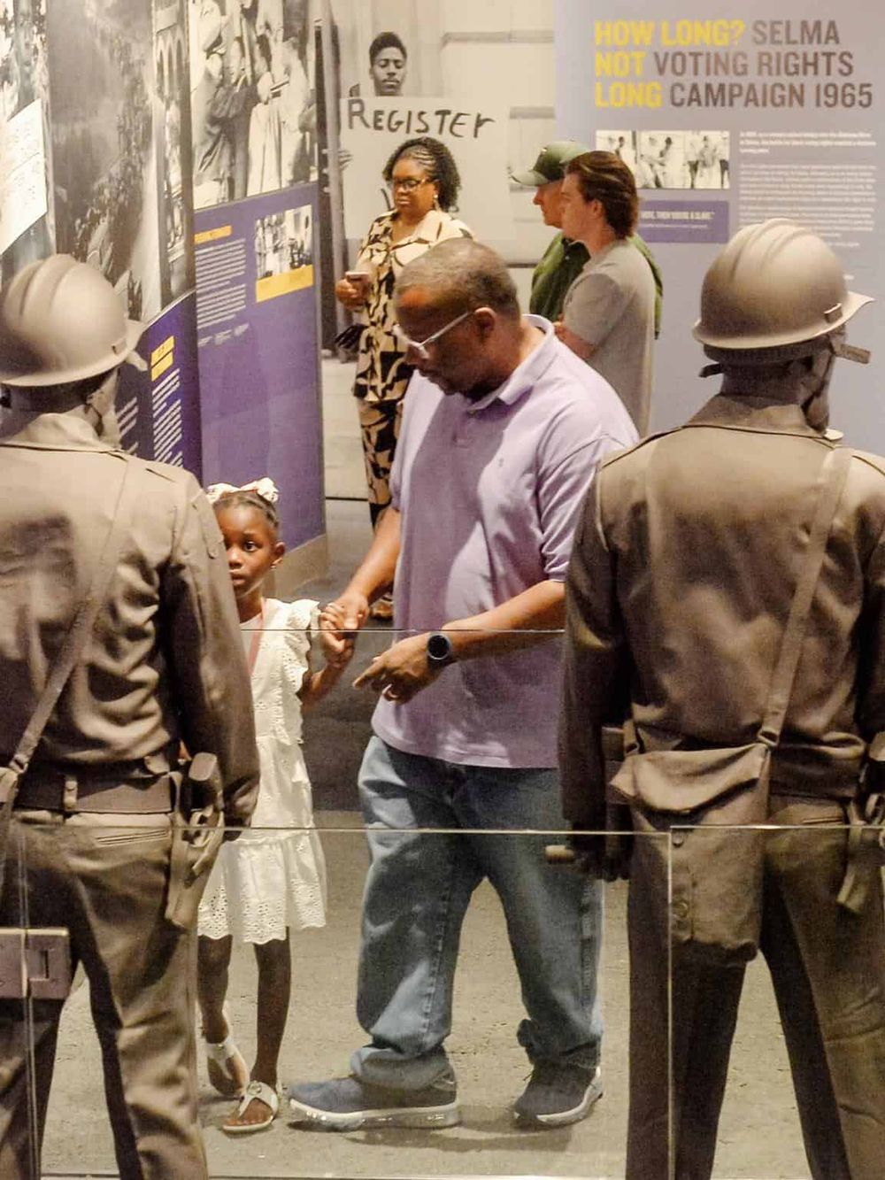 African American man holding young girl’s hand at Civil Rights exhibit with historical photos and displays.