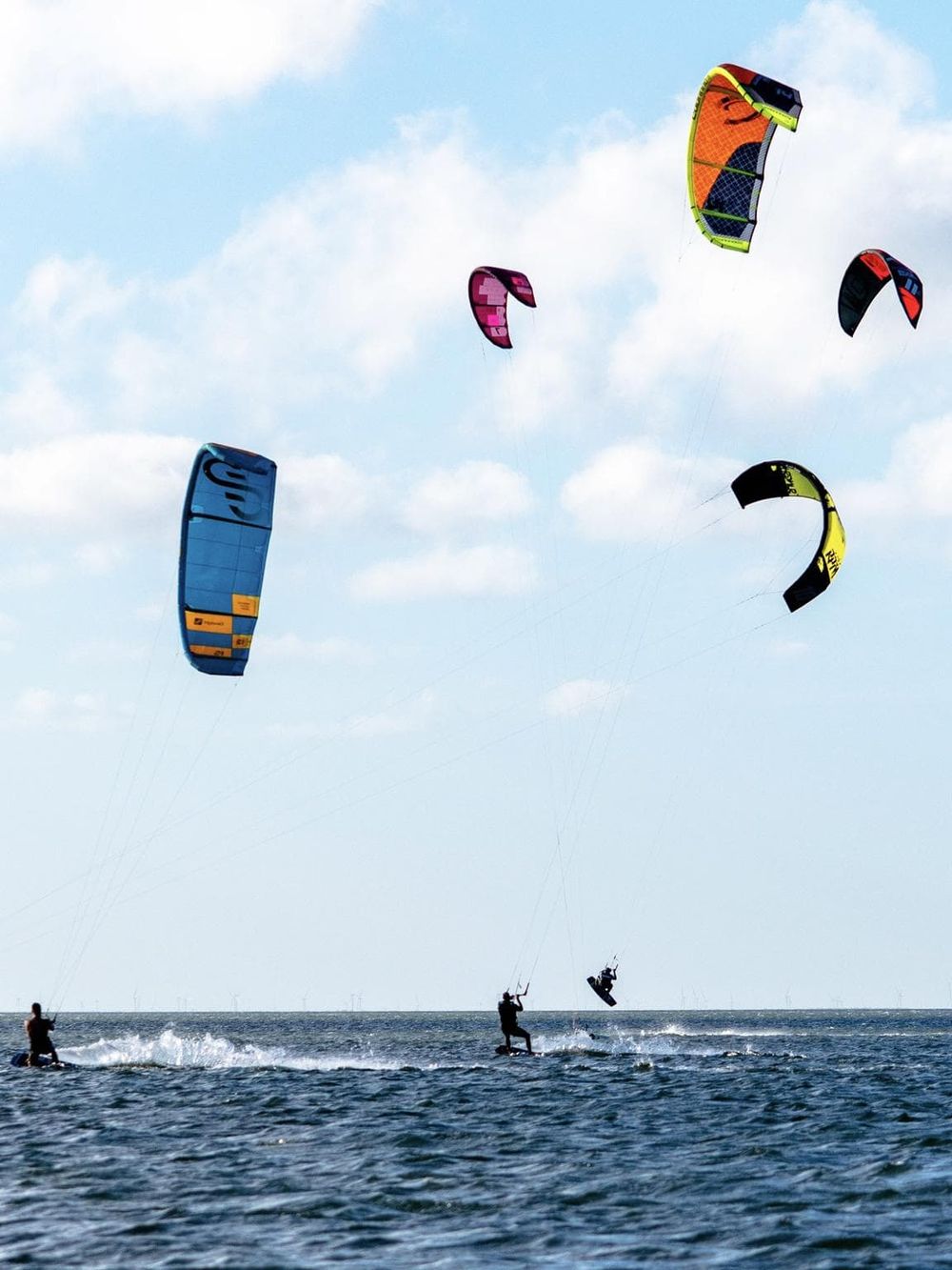 Colorful kite surfers soaring over the water on a sunny day.