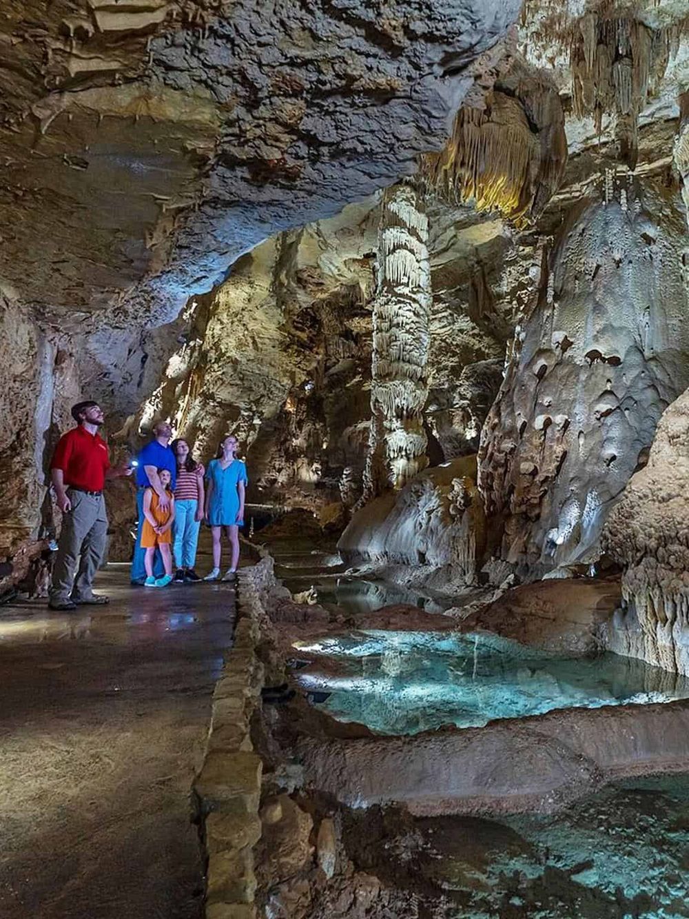 Stalactites and stalagmites inside a cave with a group of visitors exploring the underground formation.