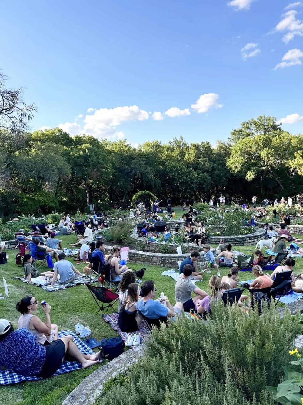 Community outdoor park with people enjoying a sunny day and lush green trees in the background.