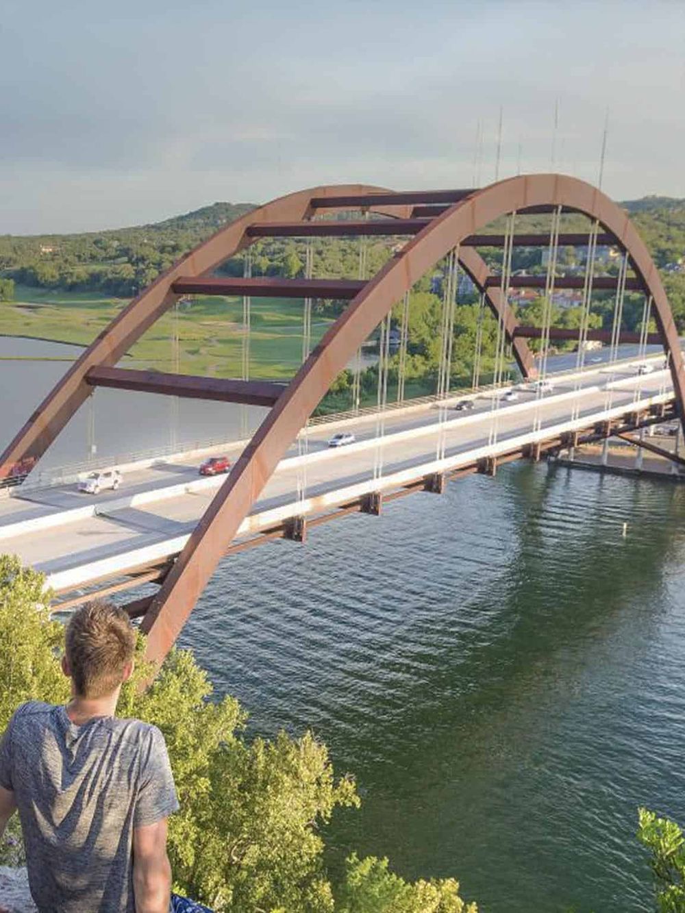 Modern arch bridge over waterway with traffic and scenic background.