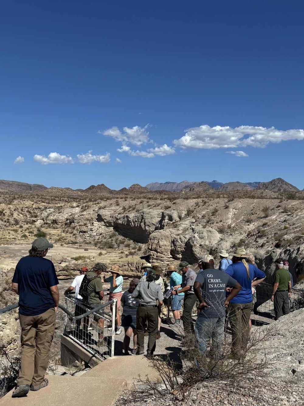 Hiking group exploring a desert canyon with rugged cliffs under a bright blue sky, ideal for adventure and outdoor exploration.