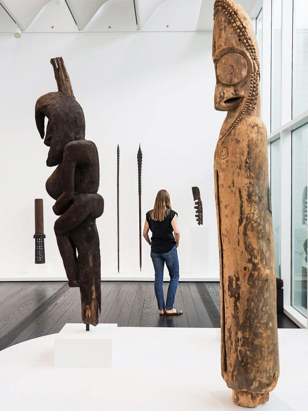 Ancient tribal wooden sculptures displayed in a modern art museum exhibit.