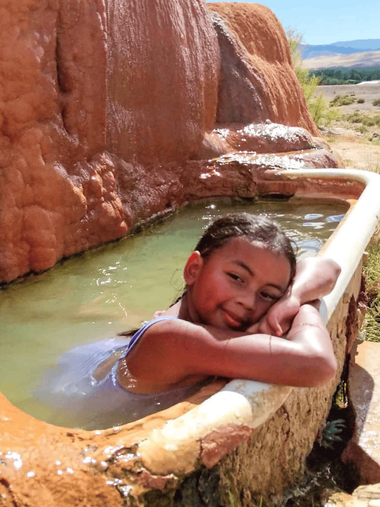 Relaxing girl in a natural hot spring surrounded by red rock formations, outdoor scenic landscape, Utah adventure travel, desert thermal baths, outdoor relaxation, nature spa, travel destination.