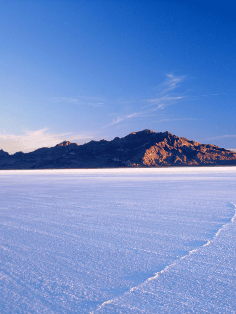 Frozen desert landscape with mountain range and clear blue sky.