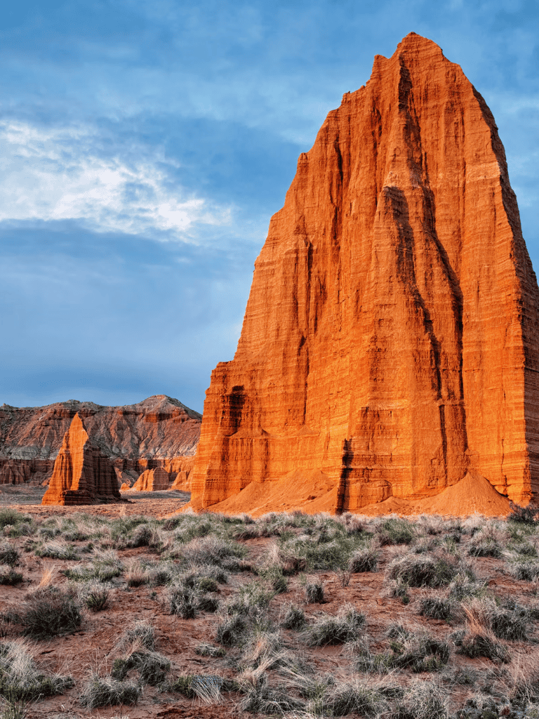 Vibrant red rock formation in a desert landscape with sparse vegetation and a cloudy sky.