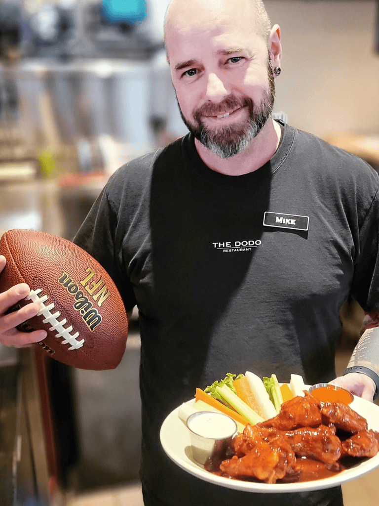 Football enthusiast chef holding plate of wings and vegetables at restaurant.