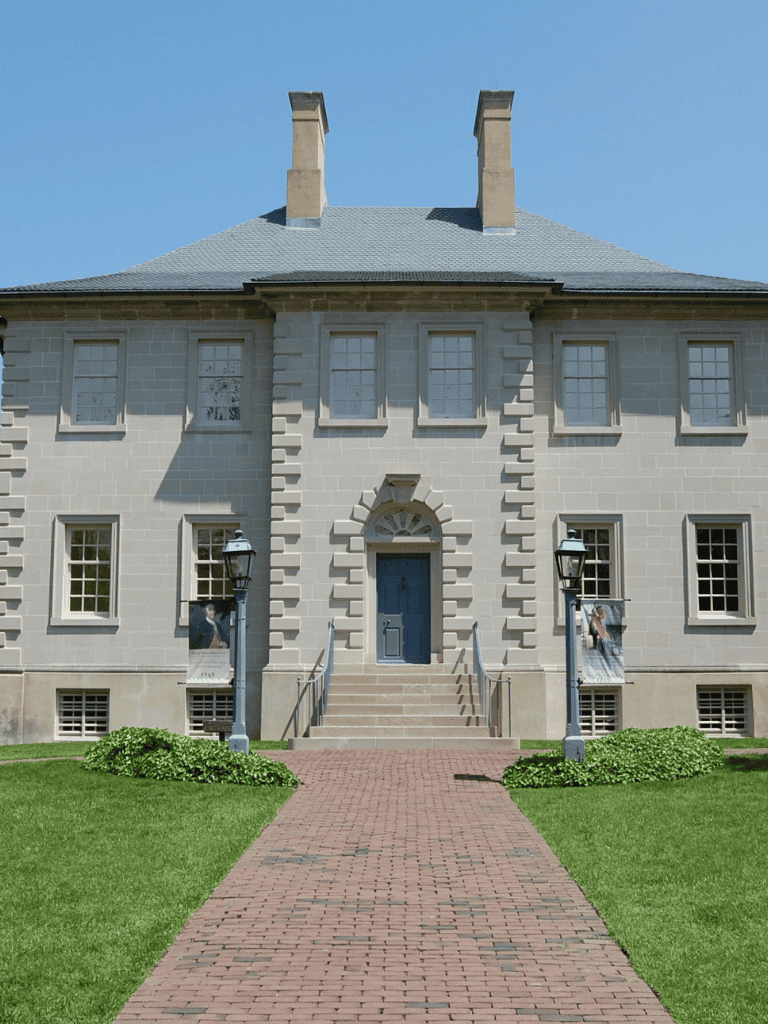 Charming historic stone house with brick walkway and lush green lawn, ideal for real estate or museum visuals.