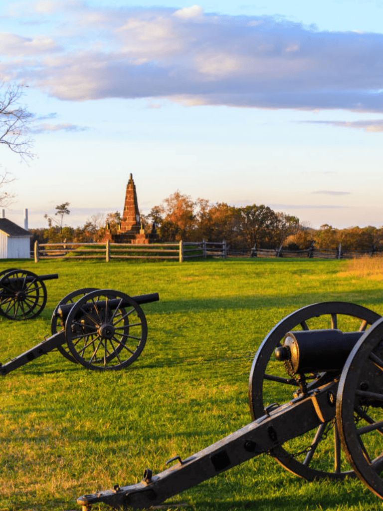 Cannons and historic monument on a peaceful battlefield at sunset.