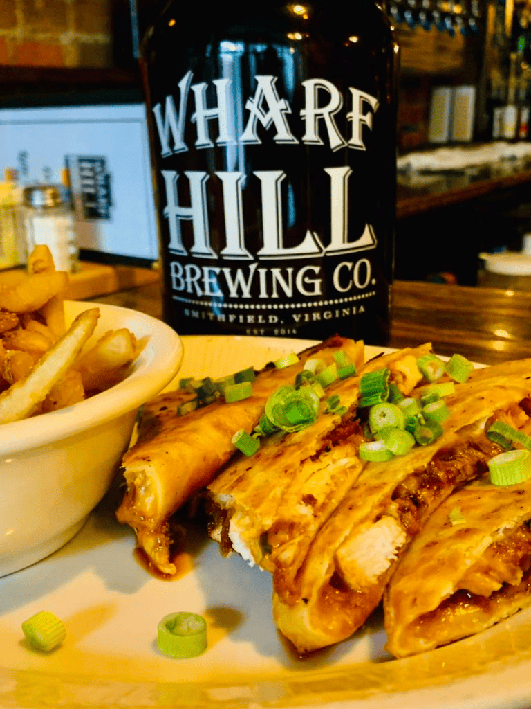 Juicy chicken wings garnished with green onions, served with crispy fries and craft beer from Wharf Hill Brewing Co.