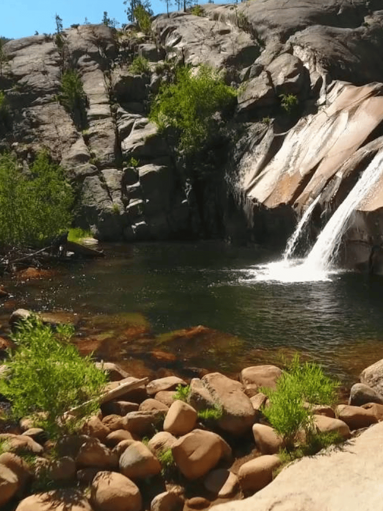 Tranquil waterfall cascading into river with rocks and greenery, scenic nature landscape.