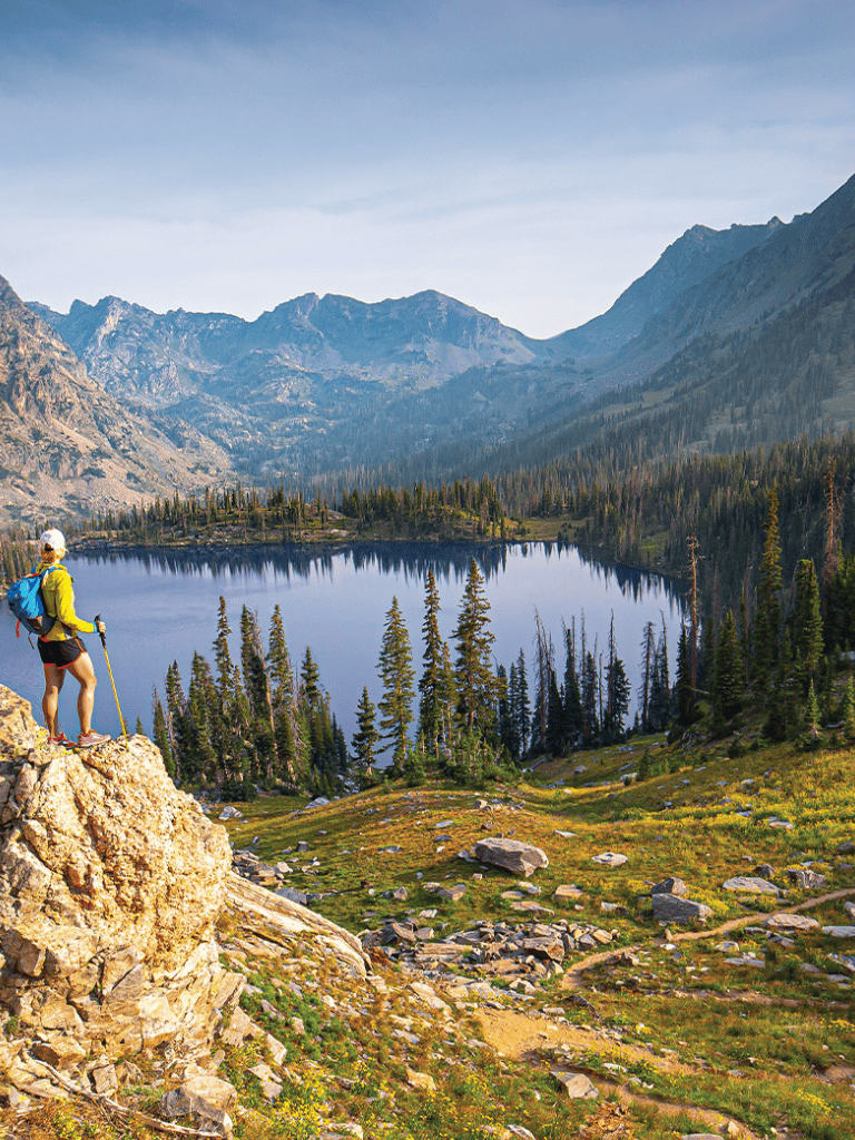 Serene mountain lake with hiker enjoying scenic views of wilderness and nature.