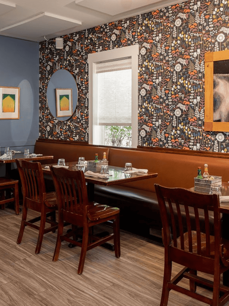 Elegant restaurant interior with floral patterned wall decor, wooden furniture, and natural light.