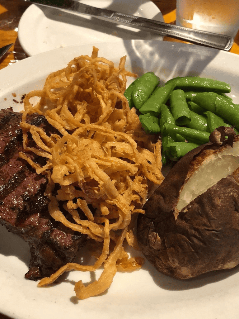 Grilled steak with crispy fried onions, green beans, and baked potato at QuestForDirections restaurant.
