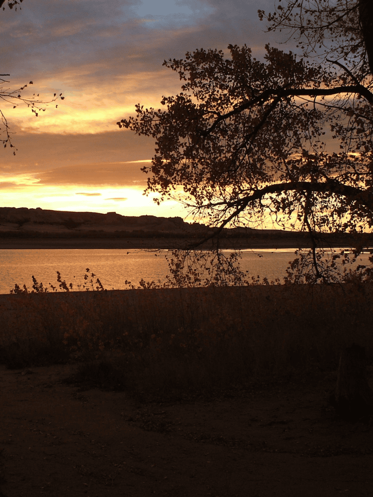 Serene sunset over a river with silhouettes of trees and distant hills, perfect for nature and outdoor adventures.