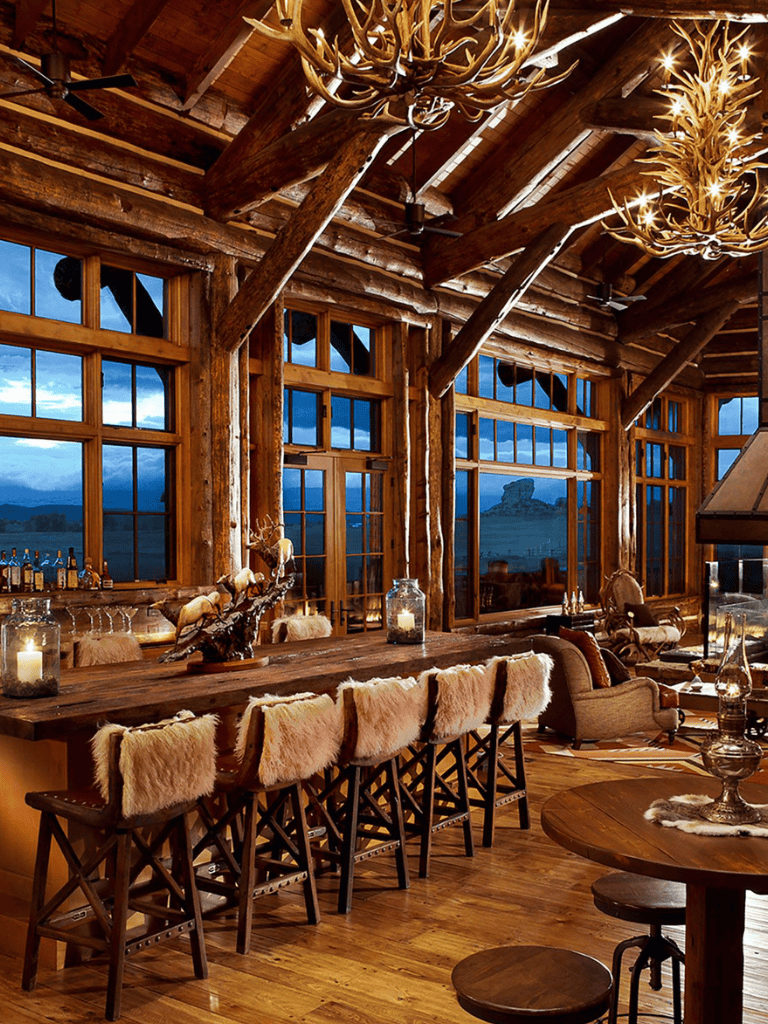 Rustic log cabin interior with large windows and antler chandeliers.