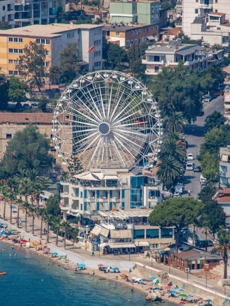 Ferris wheel at Istanbul seaside with modern buildings and beach umbrellas on shoreline.