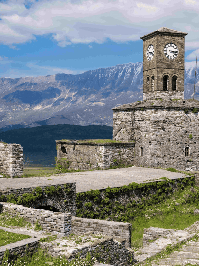 Ancient stone clock tower with mountain backdrop, historic travel destination in scenic landscape.