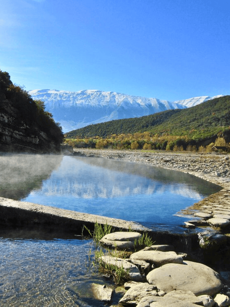 Serene riverside with snow-capped mountains in the background, showcasing natural beauty and outdoor adventure.