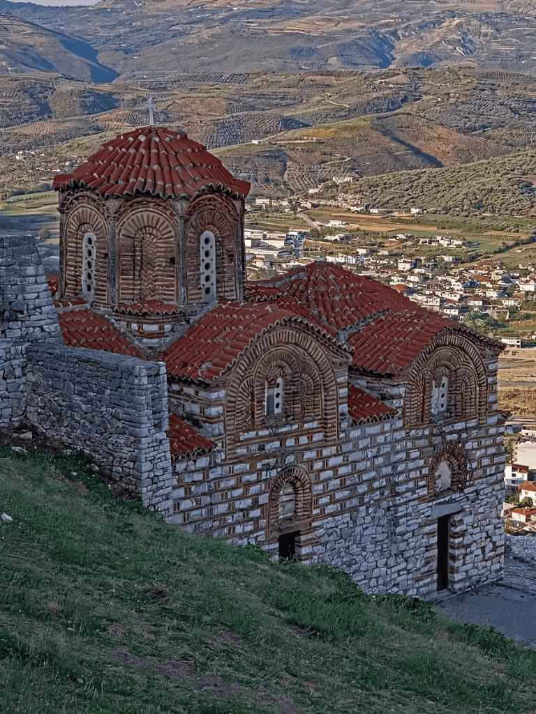 Rustic Byzantine church built with stone and red tiles, scenic mountain landscape in the background.