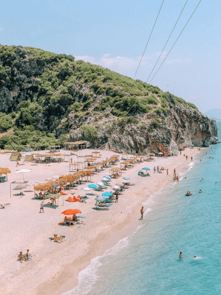 Pristine beach with colorful umbrellas, sandy shoreline, and lush green cliffs in the background.