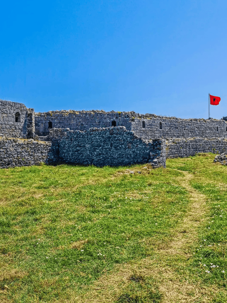 Ancient fortress with stone walls and a red flag under a clear blue sky.